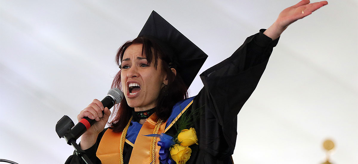 Malina spaeaking passionately into the microphone, one hand thrust toward the ceiling.