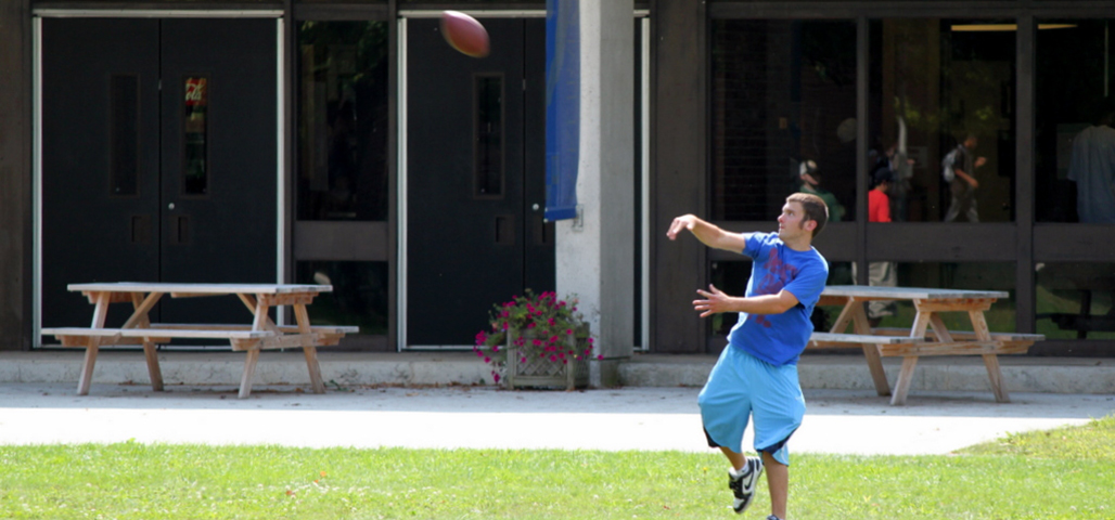 A student participating in one of the intramural student activies. He is throwing a football in front of the athletics building.