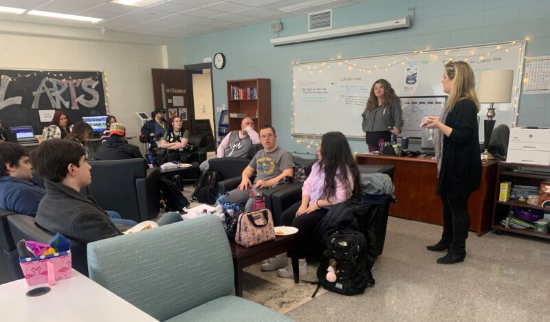 Two professors talk to a group of students who are sitting down. 