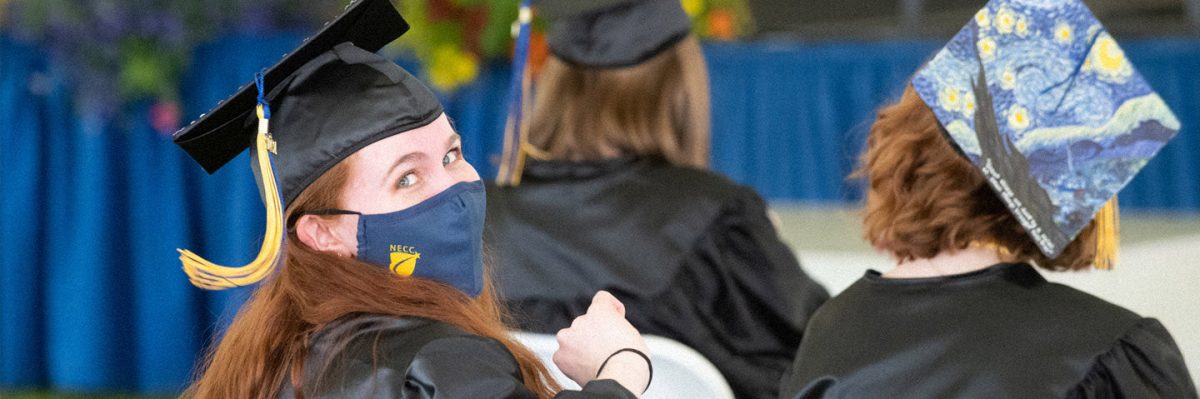 Graduate looking at camera wearing mask while sitting with other graduates