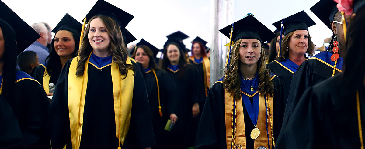 Two lines of Graduates, in graduation regalia, walking down the aisle.