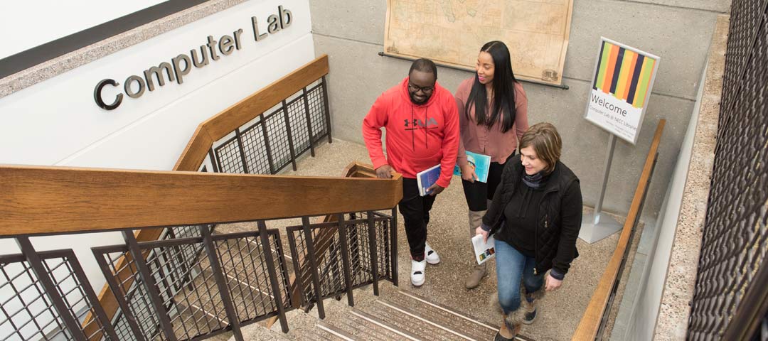 Three students walking the stairs to the Computer Labs. Welcome sign behind.