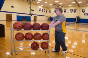 Brett rolls the basketball rack onto the court in preparation for the NECC home game.