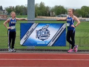 Olivia Mullins and Katelyn Richardson standing on the track by the NJCAA championship banner.