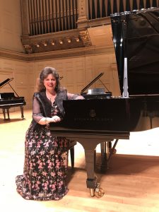 Christina Dietrich sits in a long dress at a Steinway piano