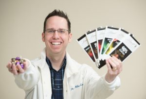 Wearing a white lab coat, Professor Mike Cross shows an array of chocolate candies in his hands