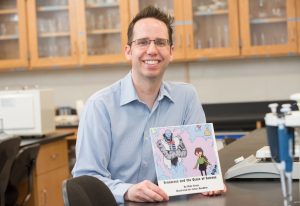 Mike Cross holding his book in a science lab.