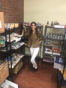 Elizabeth Mura stands next to shelving holding dry goods.