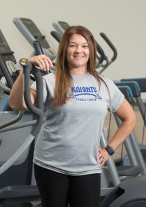 Amy Jacobs stands in the NECC Fitness Center surrounded by equipment.