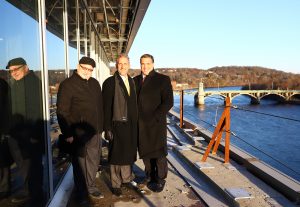 Three men stand at a railing overlooking the river.