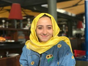 Amine Ekinci is smiling and wearing a yellow headscarf that matches the sunflowers on her denim jacket