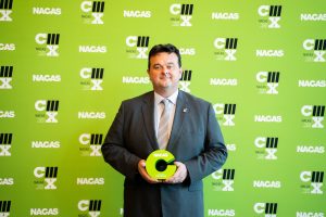 Mike McCarthy stands with a bright green award from National Association of College Auxiliary Services (NACAS)