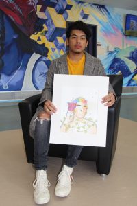 Kelvin Sabando sitting in a chair holding one of his watercolor paintings.