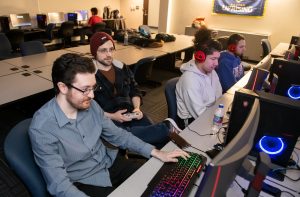 Four young men are at a long table playing video games.