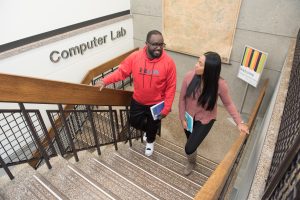 Two students, a male and a female are walking up the stairs to the computer lab.
