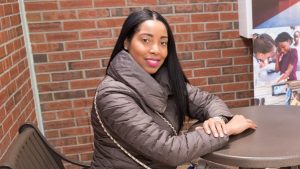 Young woman sits at table in front of brick wall.