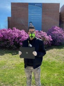 Man with face mask holds laptop computer.