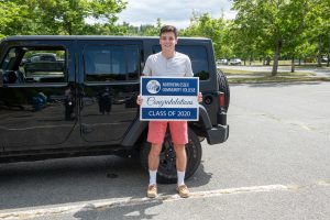 Young man stands holding NECC Class of 2020 yard sign.