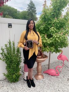 woman with long brown hair stands in backyard holding a plaque