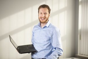 Young man stands holding laptop computer.