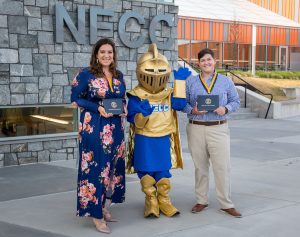 The NECC Knight mascot stands between two recently graduated women holding their diplomas.