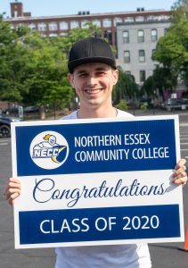 Young man in black cap holds yard sign for NECC Class of 2020