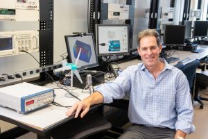 Professor Doug Leaffer is seated in an engineering lab surrounded by computers and equipment.