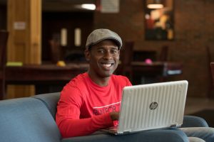 Young man in red shirt sits with laptop.