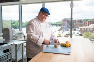 Man with glasses and wearing chef coat cuts an onion.