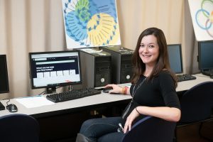 Young woman with long brown hair sits in front of a computer.