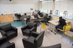 repurposed classroom with four comfortable chairs and desk with two people talking