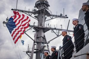 four sailors stand on a ship looking at a flag.