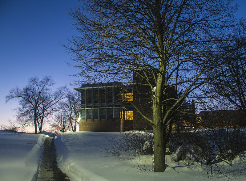 a path shoveled in white snow leading up to the technology building on the haverhill campus. it's sunset and the bare tree limbs are silhouetted against the sky