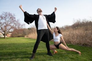 actor throwing hands in the air while actress crouches next to him, looking up admiringly