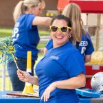 NECC Employee in blue shirt and yellow sunglasses holds pom pom