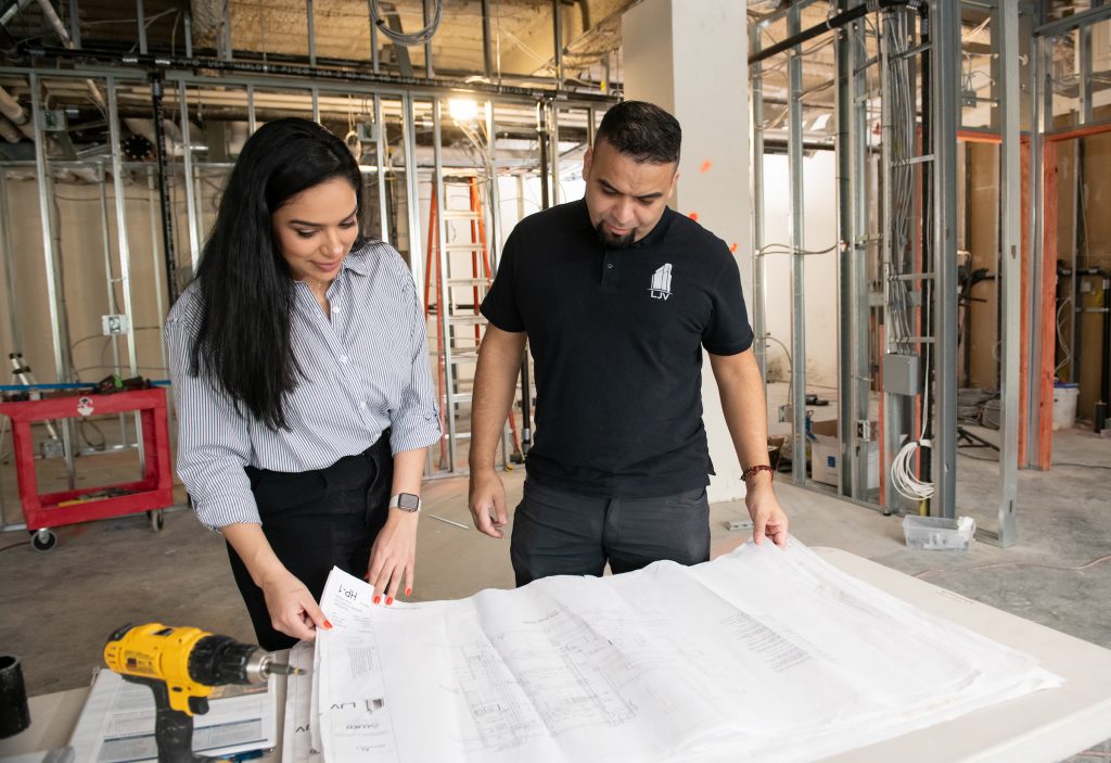 liseth looks over plans with a coworker in a room that is under construction