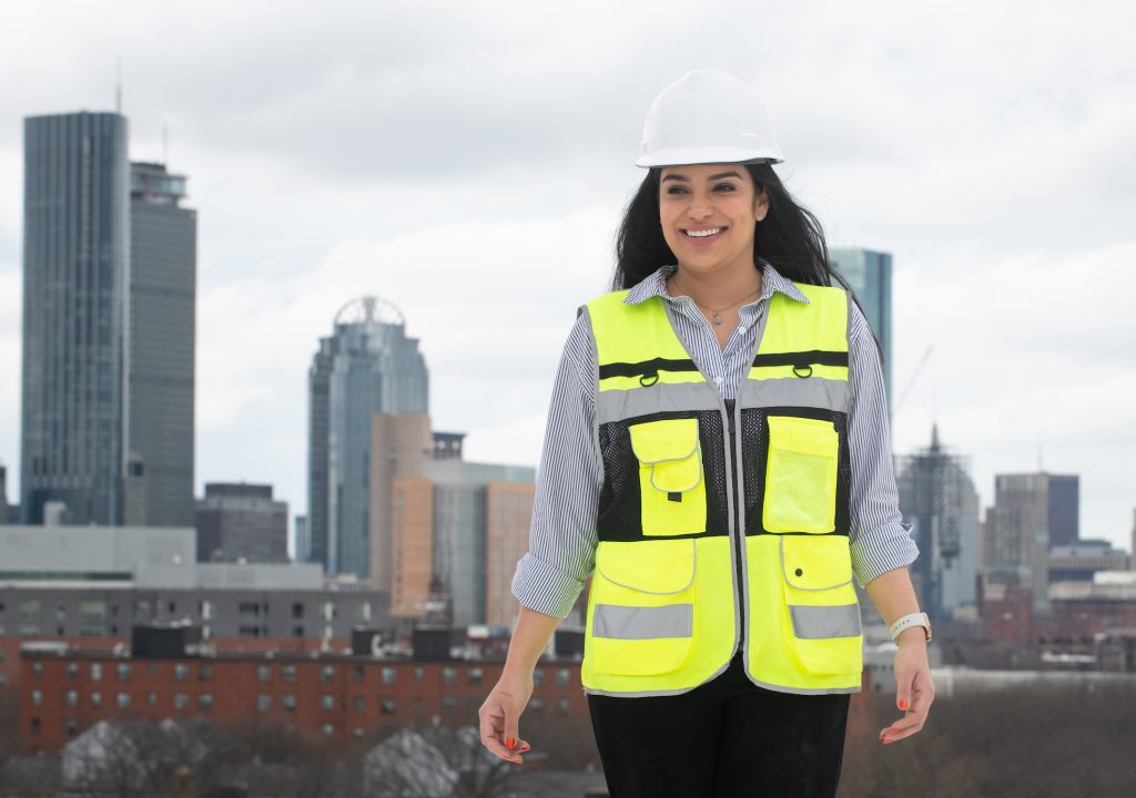 Liseth Valez wearing hard hard and reflective vest stands with sky scrapers in the background