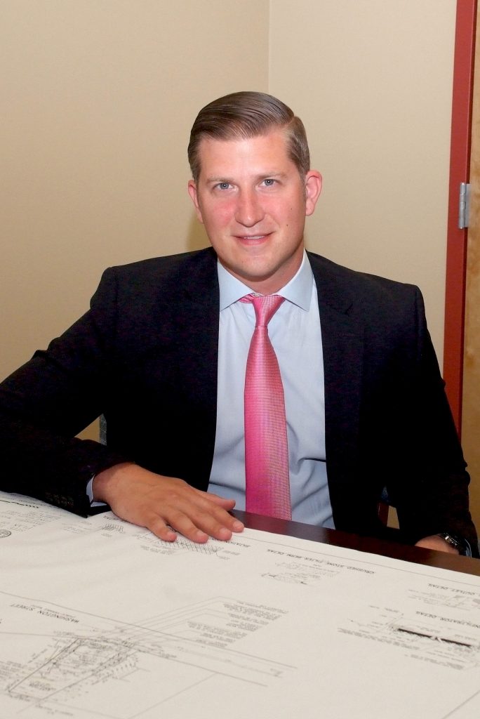 Francis J. Bevilacqua III sits at table wearing suite and red tie, smiles at camera 