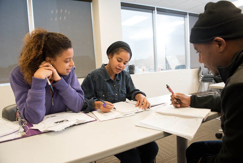 three students gather around a table with open notebooks