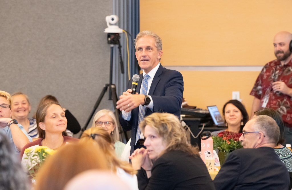 president glenn stands among a group of seated attendees with microphone