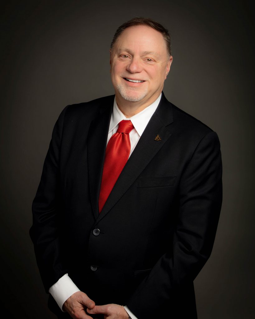 lloyd poses for the camera wearing a black suit with red tie