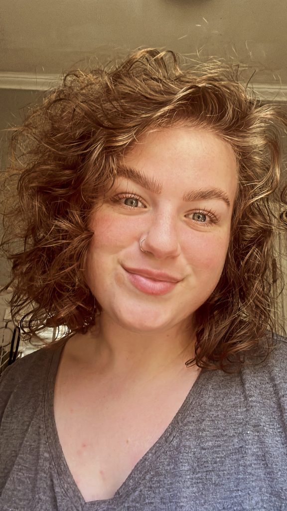 Erin Archambault smiles at the camera wearing grey, v neck shirt