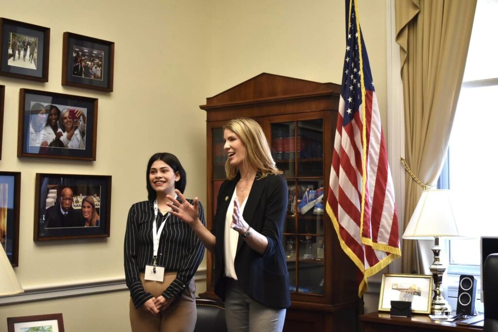 sarah stands with lori trahan in office with framed photos on the wall and american flag in the background