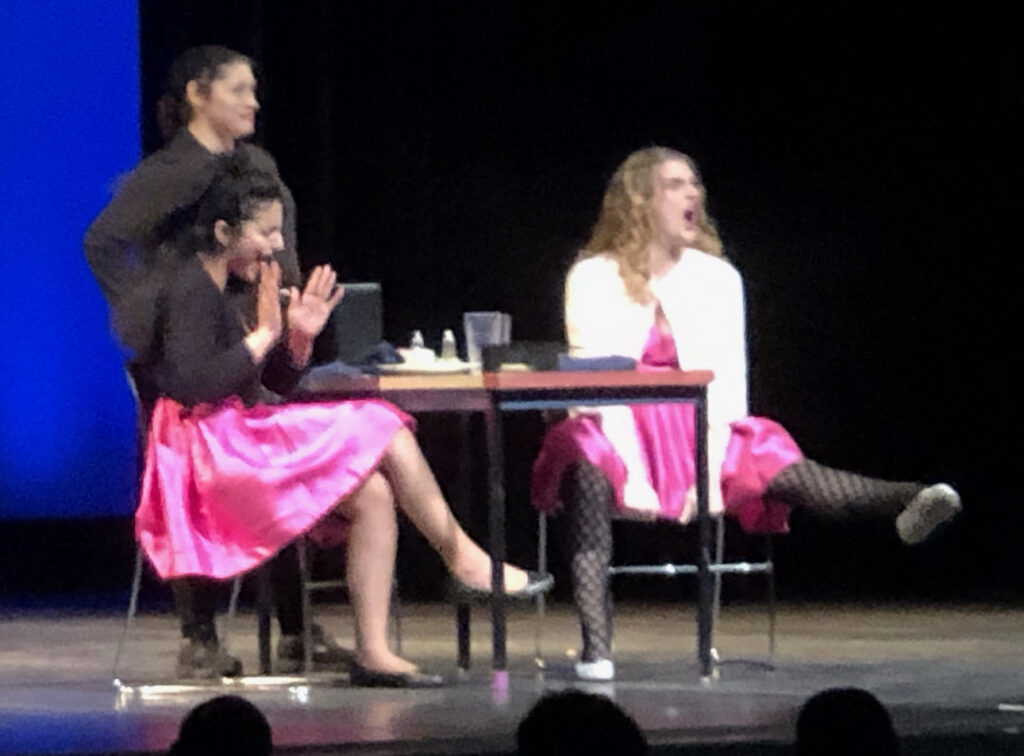 three actors sit at table wearing silk pink dresses