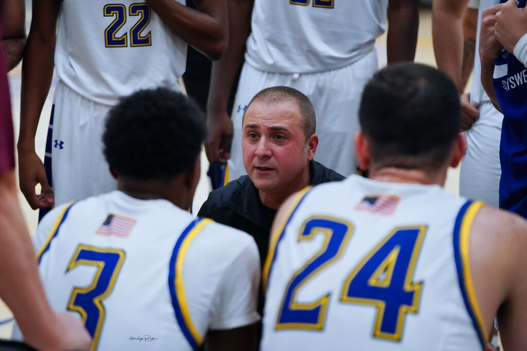 coach kneels in front of seated players, talking to them about plays