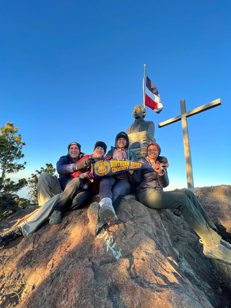 leaders pose on top of mountain holding NECC pennant 