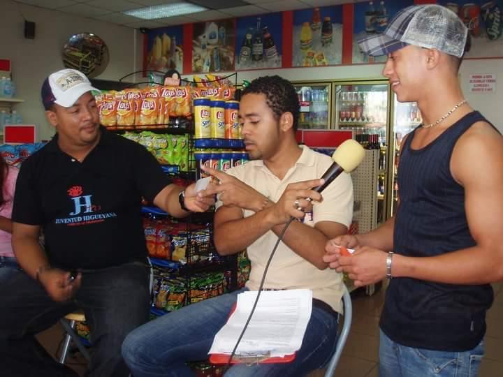 a young pedro sits on a stool interviewing two people with a microphone