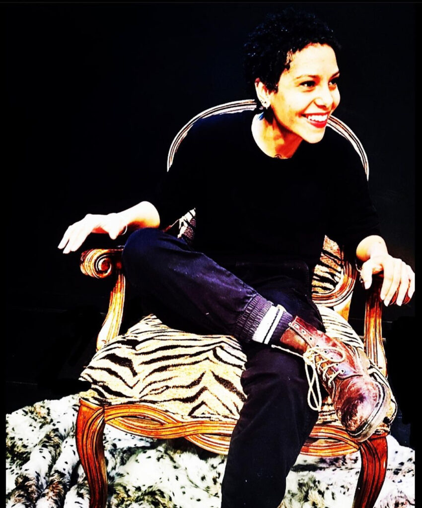 student with short cropped hair sits on a zebra print chair grinning at the audience