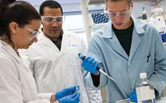 Students in lab coats and goggles pippeting something in a lab.