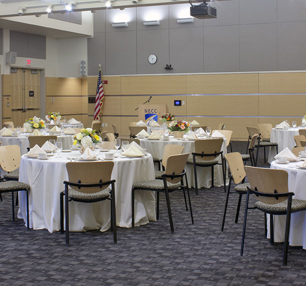 Round tables in the tech center with formal dinning settings; white floor length table clothes, and dinner settings on tables with wine glasses.